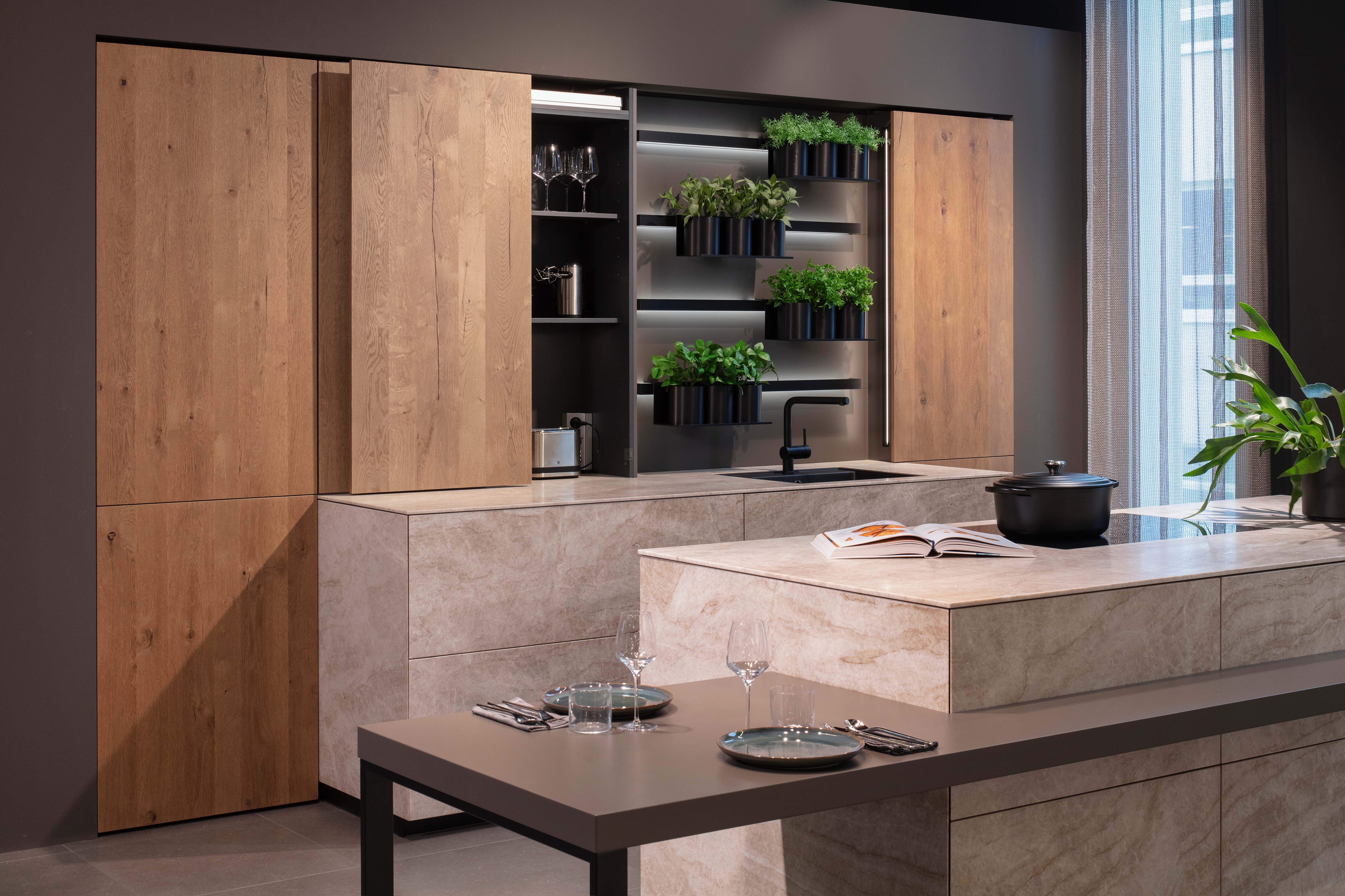 Leicht Küche mit Hochschränken in Holz und einer Kücheninsel in Betonoptik mit angesetzten Tisch