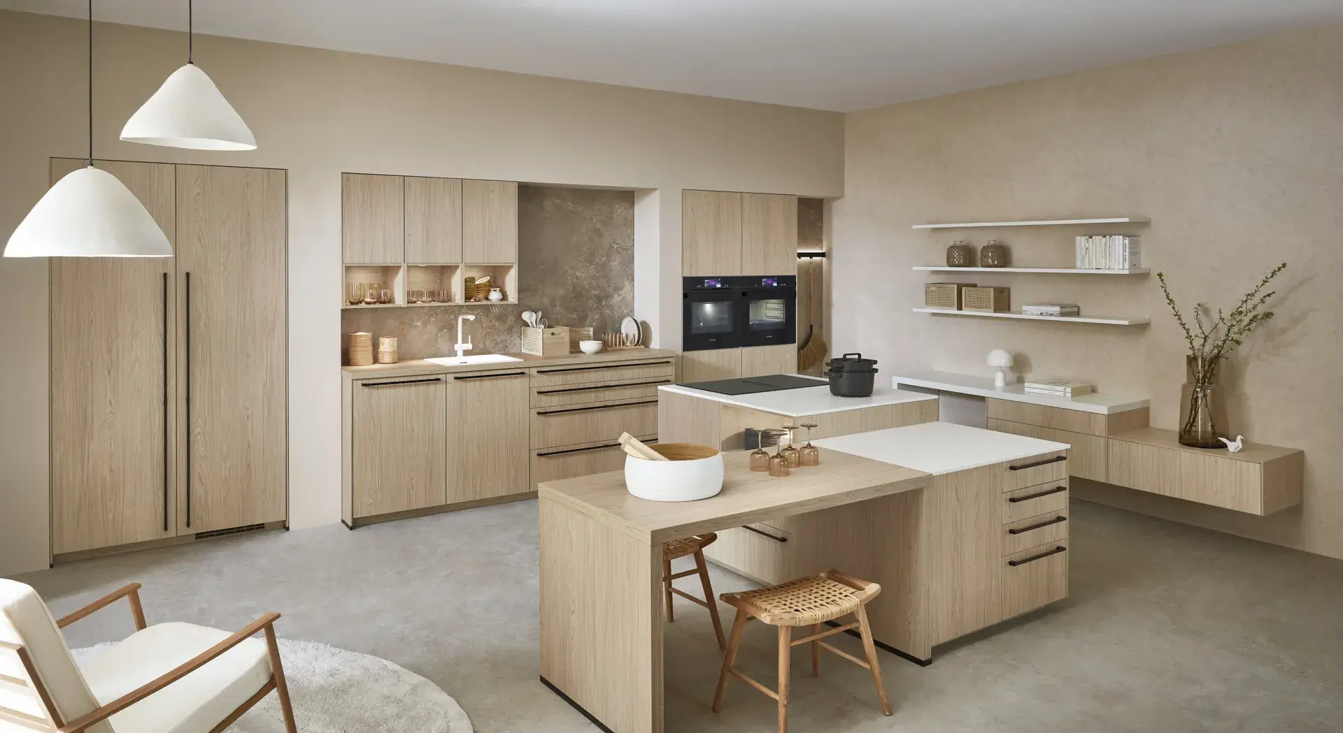 Gegenschuss, Mix aus Eichennachbildung und Premium Matt weiß, 2 Kücheninseln, eine mit Siemens Induktionskochfeld und Muldenlüfter, 2 Siemens Einbaubacköfen, Sitzbereich, 3 Oberschränke über der Spüle, Regalelement an der Wand, graue Nischenrückwand, Siemens Kühlschrank, Siemens Geschirrspüler