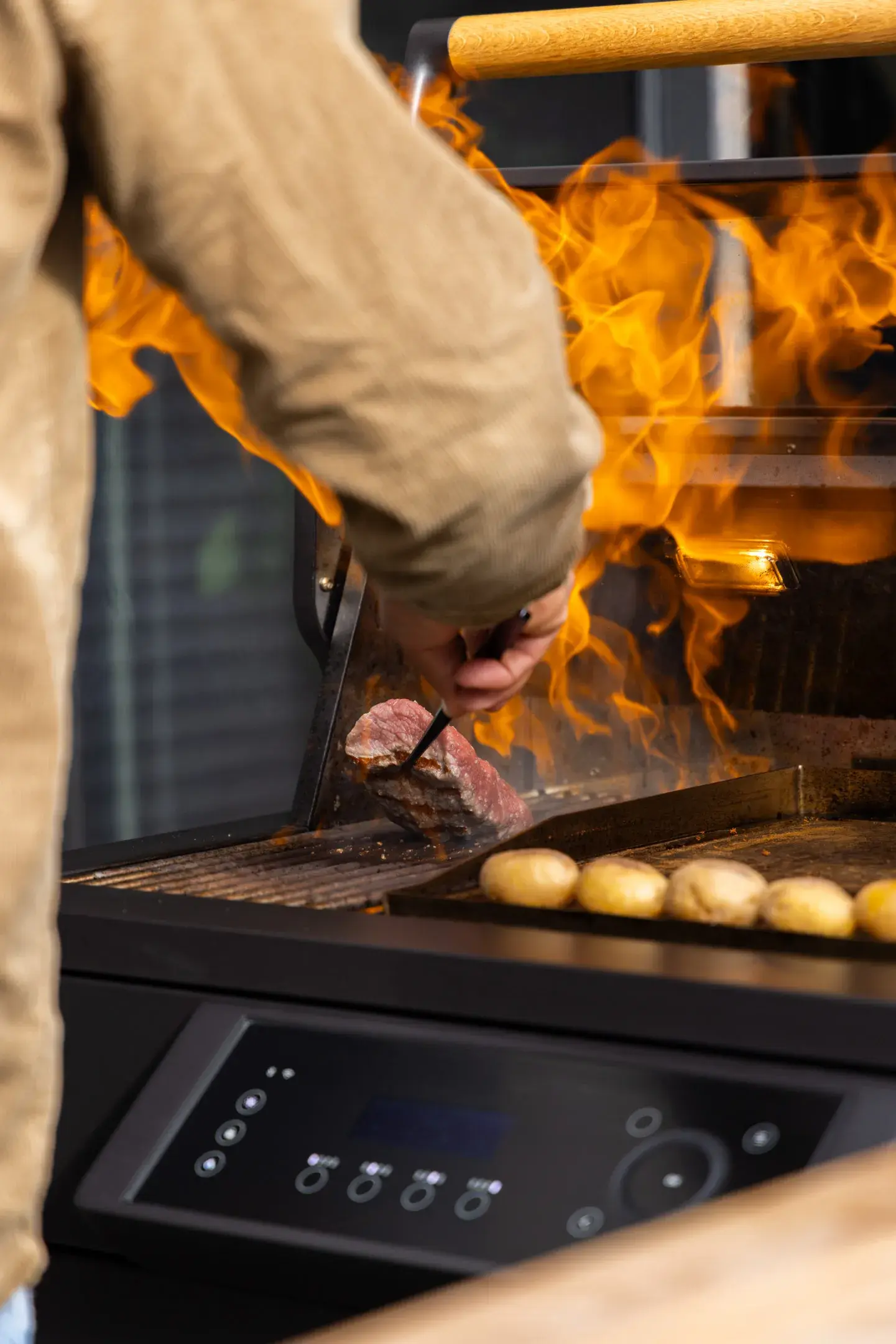 Person grillt Fleisch und Kartoffeln bei starker Flamme auf einem modernen Grill.